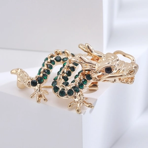 Close-up of golden dragon brooch with green rhinestones on white geometric block