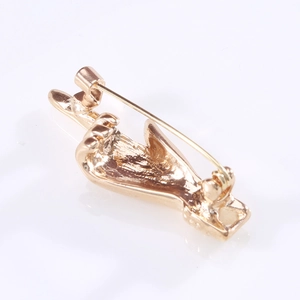 Macro detail of a polished gold-tone alloy pin in a creative middle finger gesture shape