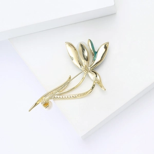 Détails d'une élégante broche magnolia dorée avec émail vert et perle blanche ronde