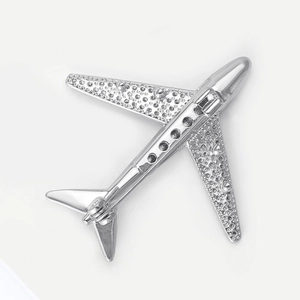 Macro detail of a polished silver aircraft brooch with textured wings on white background