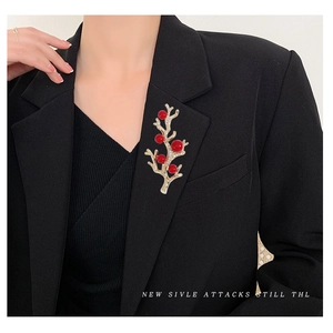Broche branche dorée avec perles rouges et zircons sur une veste de tailleur noire