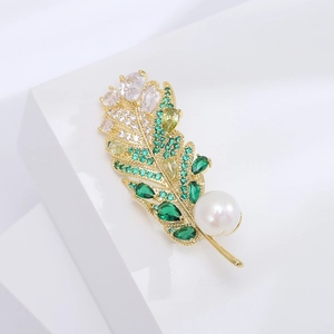 Broche plume dorée exquise avec cristaux verts et grande perle sur un support blanc