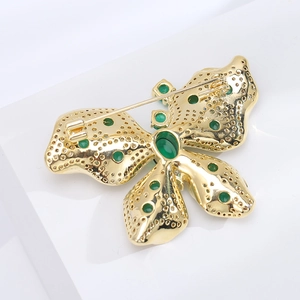 Détail macro de broche papillon avec plaquage or, zircons verts et épingle de sécurité
