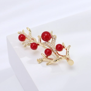 Détail d'une broche branche avec perles rouges et zircons micro-pavés sur support blanc