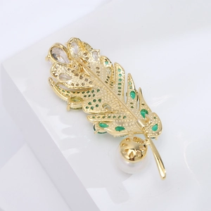 Détail de la broche plume dorée avec pierres en zircon et perle blanche élégante
