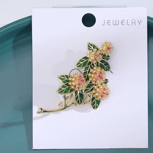 Close-up of a golden flower brooch with green enamel leaves and pink zircon crystals