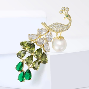 Elegant peacock brooch with green zircons and a white pearl on white background