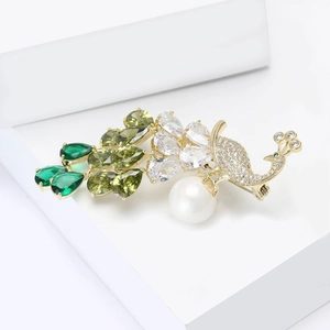 Close-up of elegant peacock brooch with green zircons, large pearl and gold plating