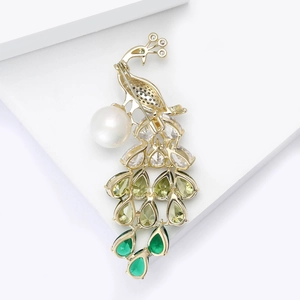 Detailed macro view of peacock brooch with green gemstones and white pearl on golden finish