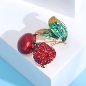 Vue détaillée d'une broche cerise en émail avec strass rouges et nervures dorées