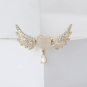 Elegant gold heart wings brooch with zirconia and teardrop pendant on white stand