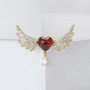 Elegant gold heart brooch with red wings and crystal drop pendant on white background