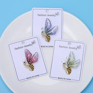 Détail de trois broches abeilles colorées avec rayures émaillées et ailes scintillantes