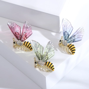 Trois élégantes broches abeilles en cristal aux ailes colorées sur un support blanc