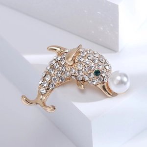 Broche dauphin dorée élégante avec strass blancs et perle sur un socle blanc