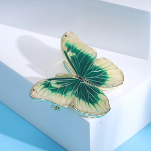 Detail view of gold butterfly brooch with green enamel wings on white platform