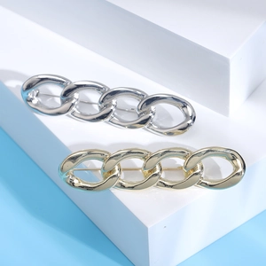 Chic chain-style metal brooches in gold and silver finish on elegant white display blocks