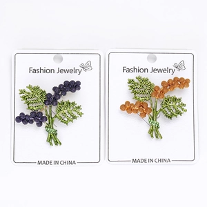 Detailed macro view of two floral cluster brooches in purple and orange on a display card