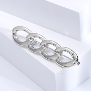 Macro shot of a polished silver chain brooch with interlocking oval rings on white blocks
