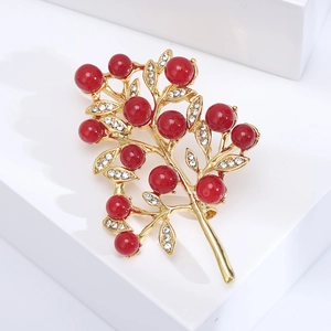 Detailed close-up of golden tree brooch with red pearl berries and sparkling rhinestones