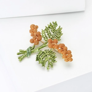 Detail of artistic plant brooch with green enamel leaves and golden bead flower clusters