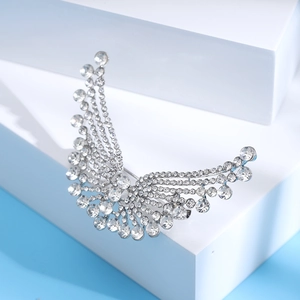 Détail d'une broche aile argentée avec strass denses sur un fond bleu clair épuré