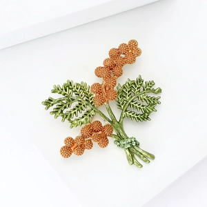 Close-up of a leaf-shaped brooch with orange clusters and green crystal details