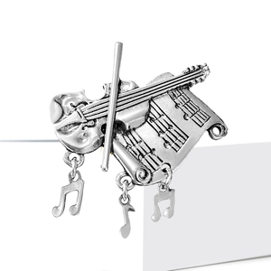 Detailed view of silver violin brooch with musical notes and bows on a white stand