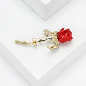 Detail of red rose brooch with gold alloy stem and leaf on minimalist white cube