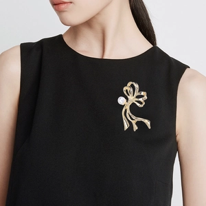 Detailansicht einer eleganten goldenen Bandschleife-Brosche mit weißer Perle am Blazer