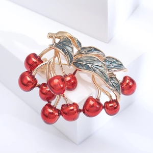Elegant red cherry brooch with gold branches displayed on a minimalist white stage
