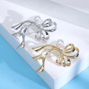 Detailansicht eleganter Band-Broschen in Silber und Gold mit Perlen auf weißem Sockel