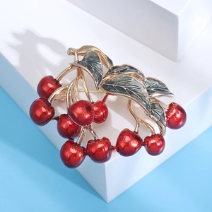 Detailed view of red cherry brooch with green enamel leaves on a gold alloy base
