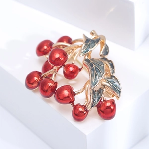 Golden cherry brooch with vibrant red enamel and green leaves on a white stand