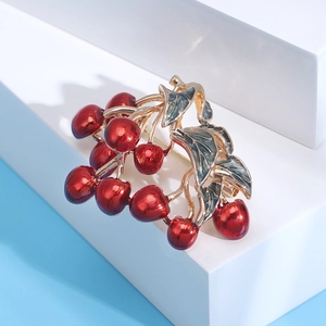 Detailed macro view of cherry brooch with red enamel and green leaves on gold alloy