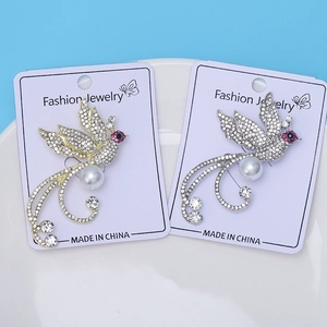 Détail de la broche phénix avec strass et perle sur carte de présentation