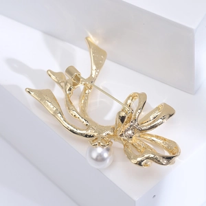 Detailansicht einer goldenen Schleifenbrosche mit Hammerschlag-Textur und Perle