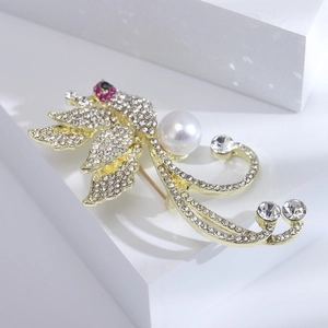 Détail d'une broche phénix avec placage à l'or, strass brillants et une grande perle blanche