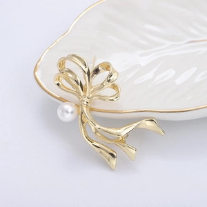 Eleganter goldener Schleifen-Brosche mit Perle auf einer weißen Keramik-Tablettschale