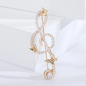Detailed close-up of golden G-clef brooch with pearls and butterflies on white pedestal