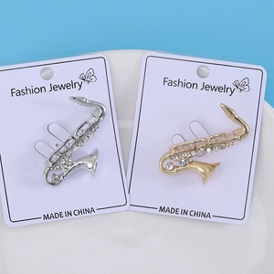 Dettaglio di spille a sassofono in oro e argento con strass lucidi su cartoncino bianco