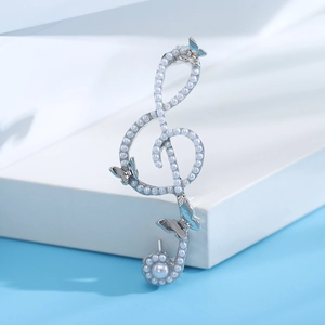 Detail of silver treble clef brooch with pave pearls and delicate butterfly accents