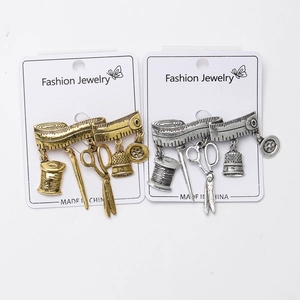 Detail of vintage sewing tool brooches with dangling tape, spool and scissors icons