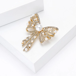 Detailed view of golden bow brooch with sparkling crystals and elegant white pearls