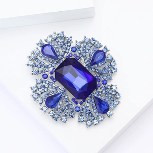 Dettaglio ravvicinato di una spilla di lusso in lega con cristalli blu su piedistallo bianco