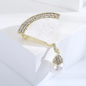 Detailansicht einer goldenen fächerförmigen Muschelbrosche mit Strasssteinen und einer Perle