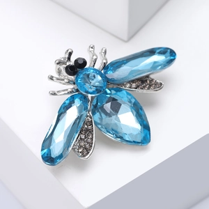 Detailed close-up of a silver bee brooch featuring blue crystals on a geometric stand