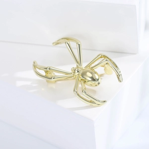 Macro shot of a polished gold spider brooch with smooth metallic finish on white blocks