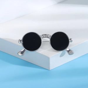 Detailed macro view of silver round sunglasses brooch with inlaid crystals on blue backdrop