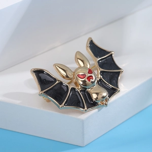 Detailed view of gothic bat brooch with black enamel, blue glitter, and red eyes on gold base